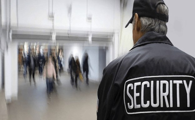 Security officer in a jacket marked SECURITY watching a busy walkway